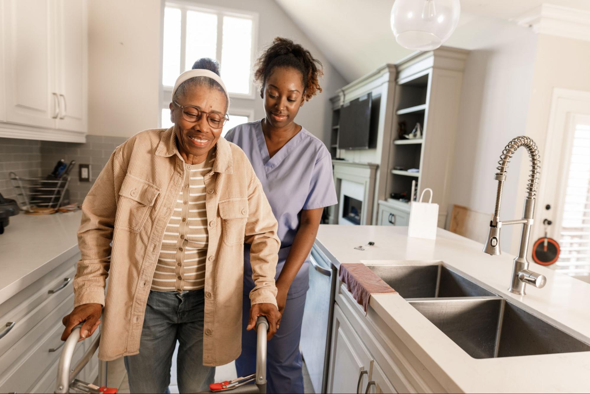 Nurse providing in home health care to patient using walker in kitchen